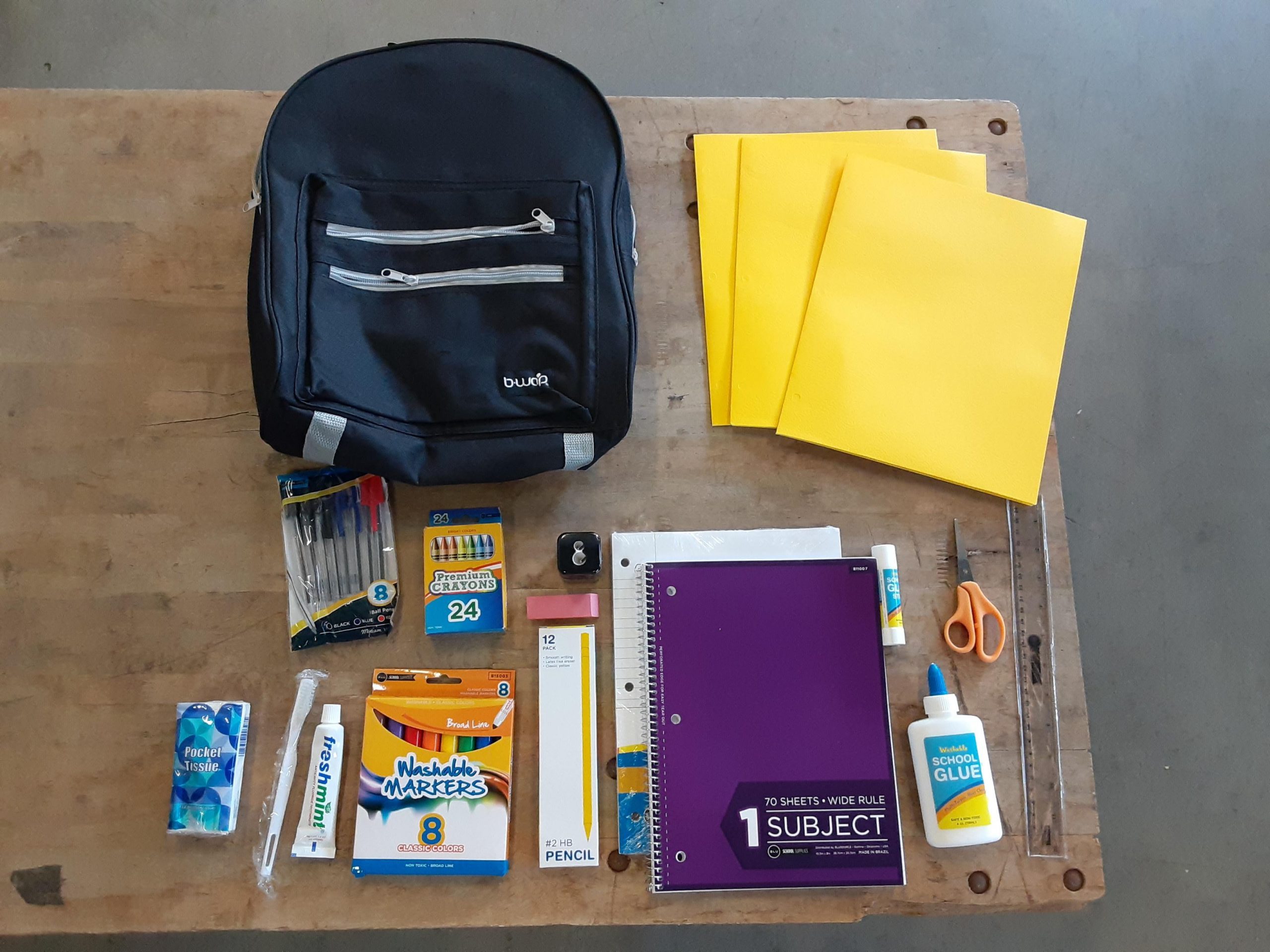 Backpack and contents displayed. Contents: folders, lined paper, spiral notebook, glue, scissors, glue stick, ruler, pencils, pencil sharpener, large eraser, crayons, markers, pens, tissues, toothbrush and toothpaste.
