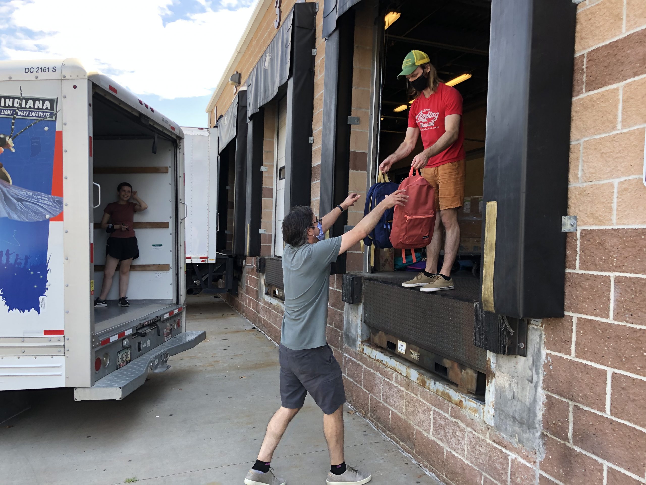 Two volunteers at the loading dock passing backpacks to be loaded into a U-Haul truck.